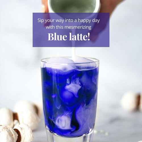 Glass of blue latte made from butterfly pea flower tea caffeine free with milk swirls on marble surface