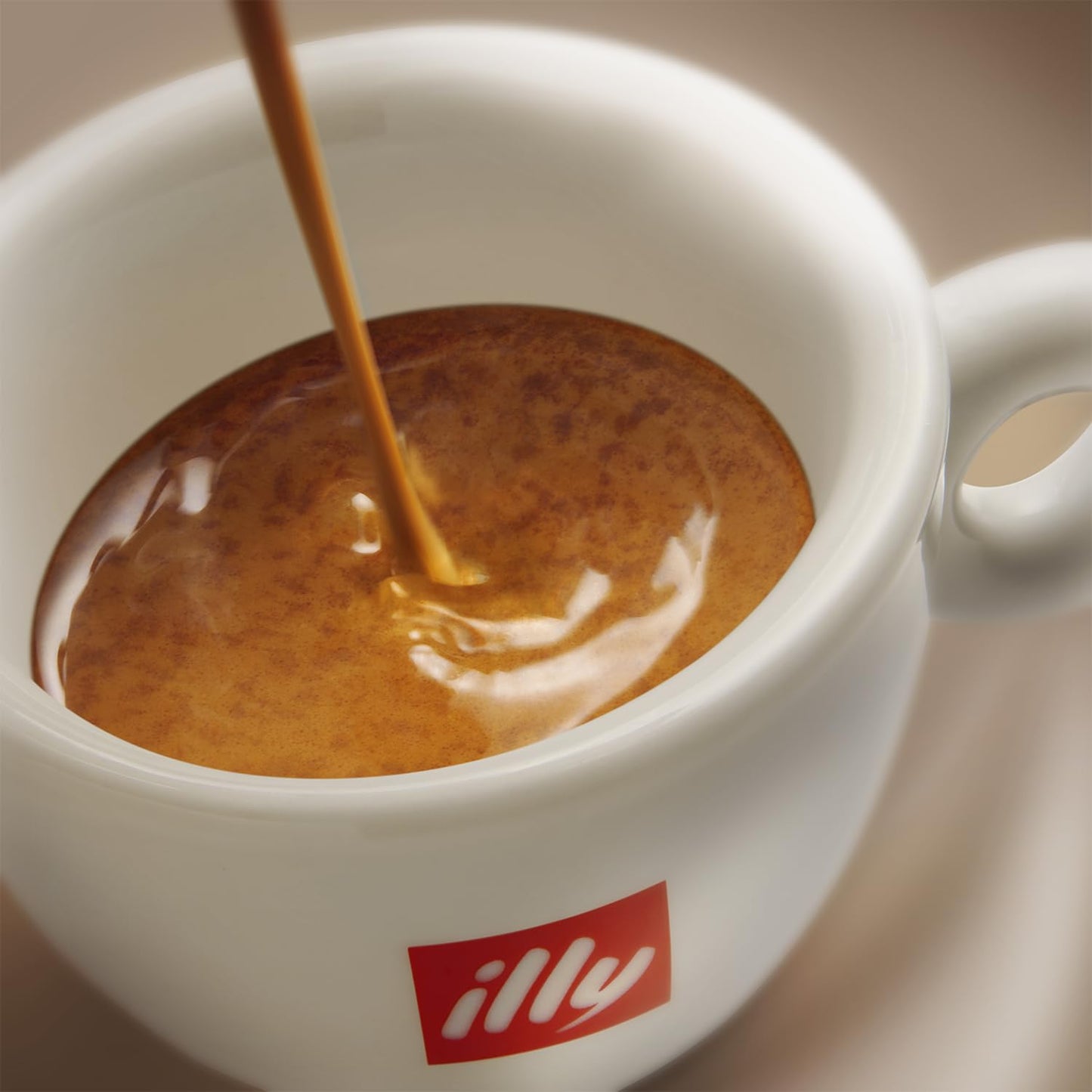 Close-up of a white cup with illy logo filled with rich crema from Illy ground espresso coffee