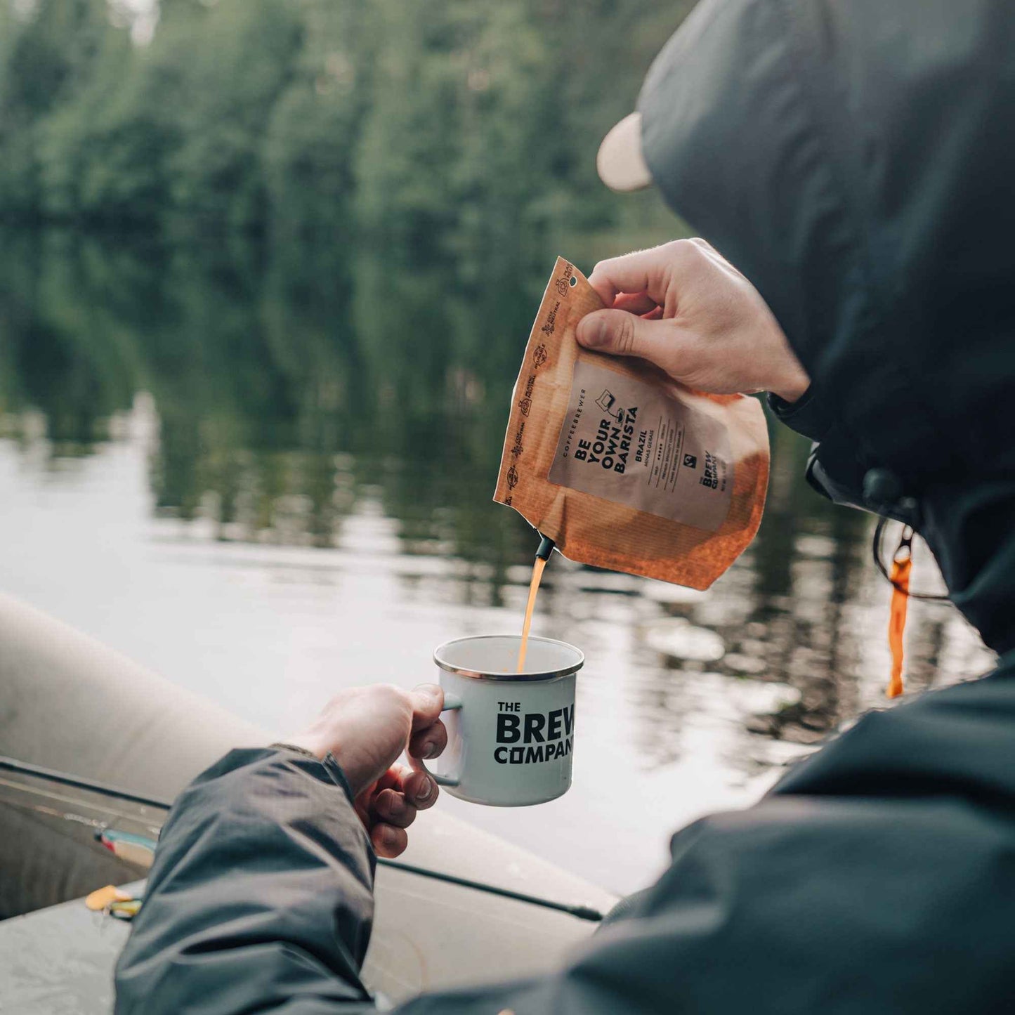 The Brew Company 25 piece coffee taster set being poured into a branded mug outdoors near a lake