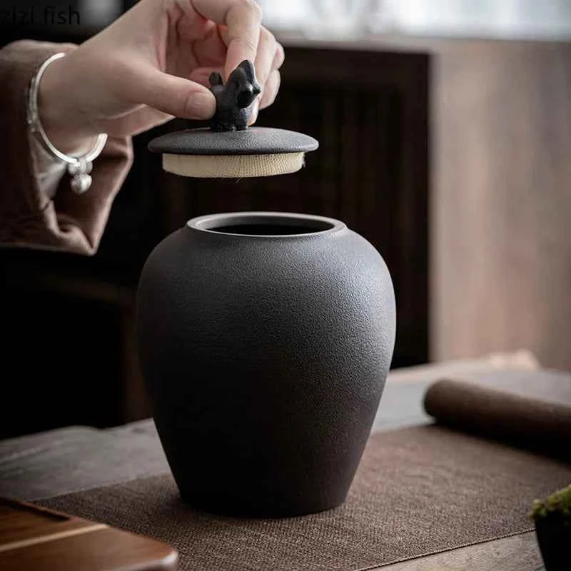 Black sealed tea storage jar with textured surface and removable lid held by hand on wooden table