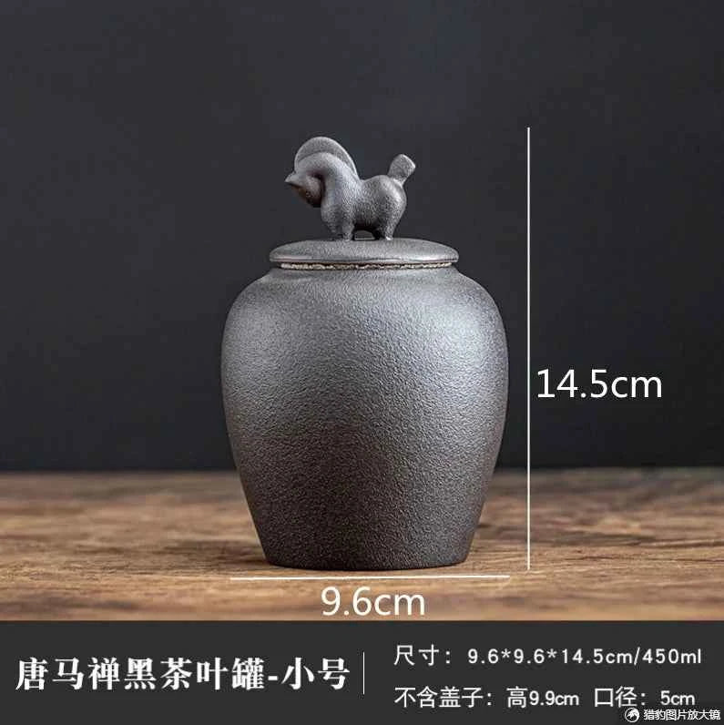 Black sealed tea storage jar with rooster-shaped lid handle measuring 14.5cm height by 9.6cm width