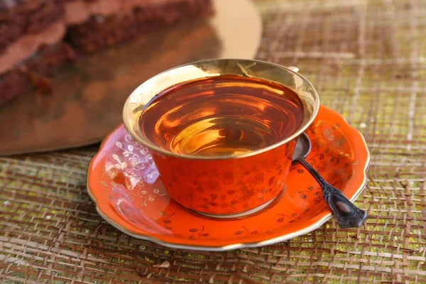 Cup of premium black teas with rich amber color served in an elegant orange and gold teacup on a textured surface