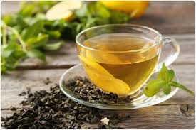 Premium organic green tea served in a glass cup with loose tea leaves and fresh green leaves on wooden surface