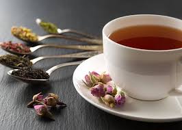 Cup of herbal tea with dried flowers and various organic herbal teas on spoons displayed