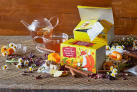 Organic wellness teas collection featuring herbal blends in yellow boxes with glass teapot and fresh flowers on wooden table