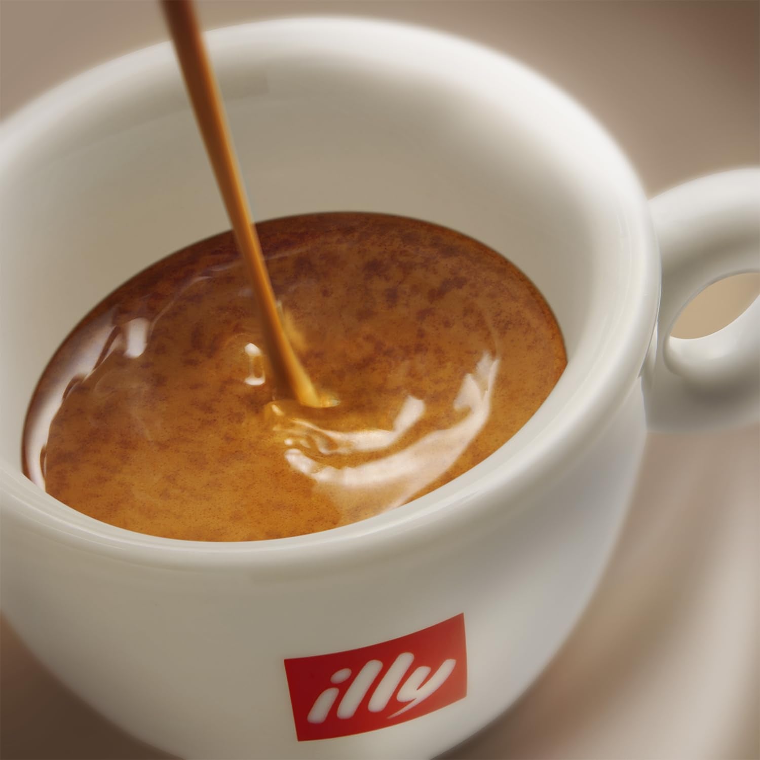 Close-up of a white cup with illy logo filled with rich crema from Illy ground espresso coffee